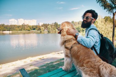 Arkadaşlarım kavramı - insan ve hayvan arasındaki. Görüş açısı, sarılma, dokunarak ve parkta, sandalyeye Gölü nün manzarayı köpeğiyle oturan genç adam