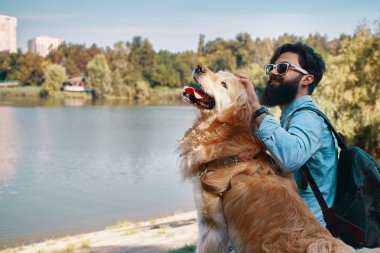 Arkadaşlarım kavramı - insan ve hayvan arasındaki. Görüş açısı, sarılma, dokunarak ve parkta, sandalyeye Gölü nün manzarayı köpeğiyle oturan genç adam