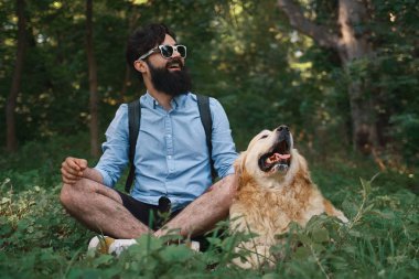Yakışıklı adam çimlere oturup istirahat gülümseyen ve mükemmel bir gün zevk ile onun sevimli köpek, bacak bacak. İnsan ve hayvan arasındaki dostluk. Mutlu arkadaş.