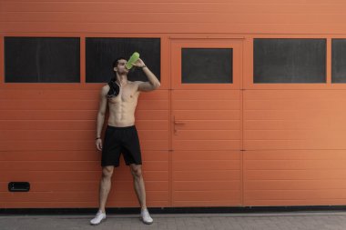 Spor modeli adam, çıplak gövde, omuz forması, içme suyu kopya alanı turuncu duvar zemin üzerine bir plastik şişe.