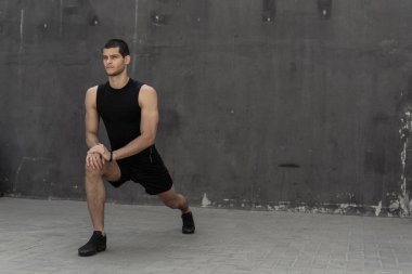 Yakışıklı, atletik bir adam önce arka planda gri duvarlar ile eğitim germe ısınma. Sağlıklı yaşam ve spor giyim reklam.