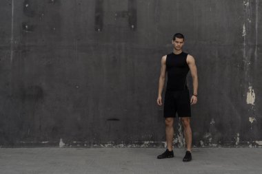 Spor giyim, endüstriyel gri arka plan üzerinde poz içinde atletik kas genç adam portresi. Şık uzun boylu erkek, spor modeli, kaslı vücut şekli, sağlıklı yaşam reklam.