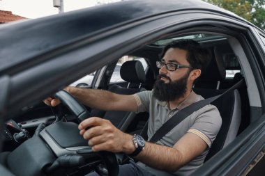 Açılı yan modern rahat sakallı adamın, Gözlük, saat ve T-shirt, arabayı kullanan giydiğini göster. Sürücülerin eller yukarı kapatın.