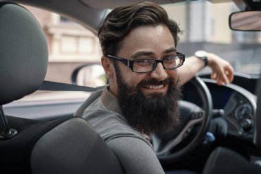 Onun yeni araba sürme. Arabasını ve gülümseyen, şehirde yakışıklı genç sakallı adam yan görünüm