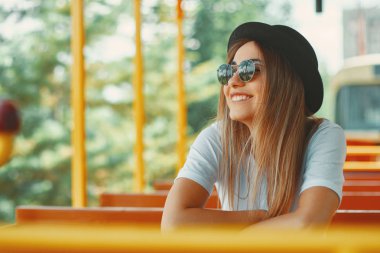 Close-up cool hipster student woman wearing eyewear glasses. Caucasian female with hat travelling on a city tour transportation watching the views, looking at camera, smiling happy. clipart