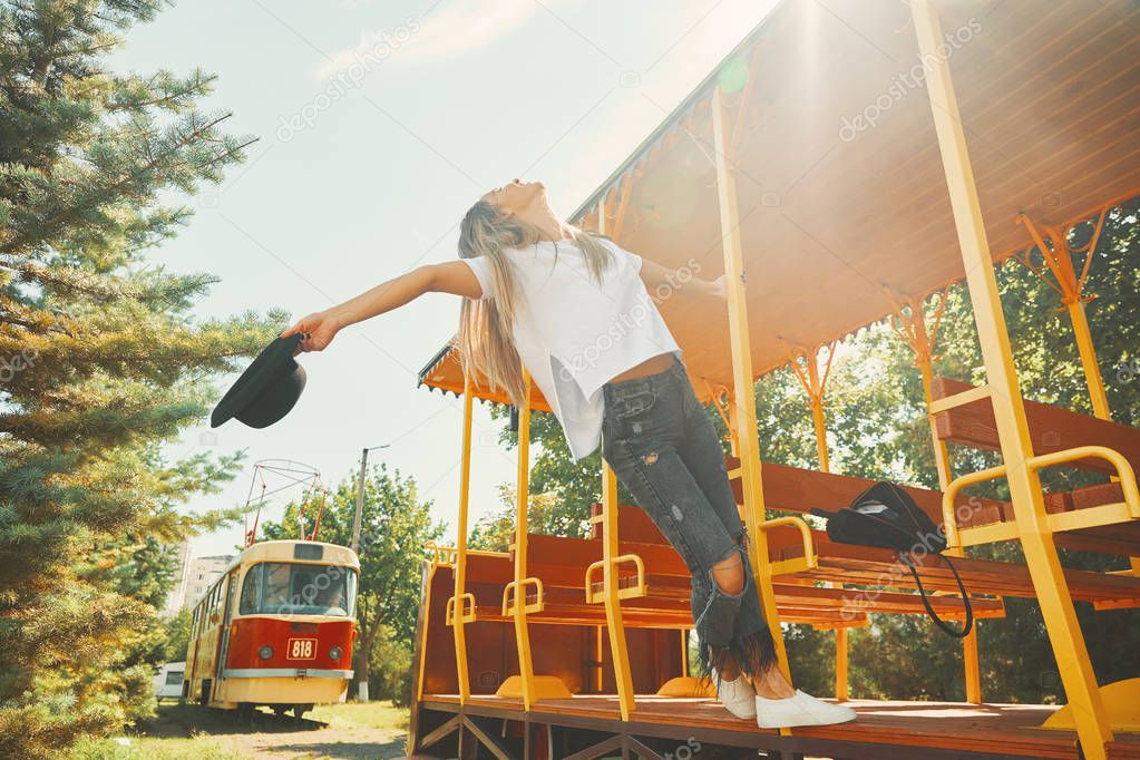 Freedom and Youth concept. Carefree fashionable young woman enjoying summer, traveling, sunlight. A stylish hipster female wearing ripped gray jeans, hat and white cropped tshirt hanging out.