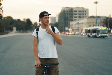 City Road, sokak uzakta içinde belgili tanımlık geçmiş city ile bisiklet sürme genç bir adam portresi. Erkek ile beyaz gömlek, kap, hedef için Bisiklete binme sırt çantası siyah bisikletle. Sağlıklı yaşam konsepti