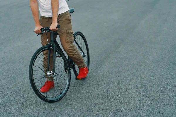 特写的休闲男子腿骑经典自行车在城市灰色的道路上穿着红色运动鞋和舒适的裤子 复制空间 — 图库照片