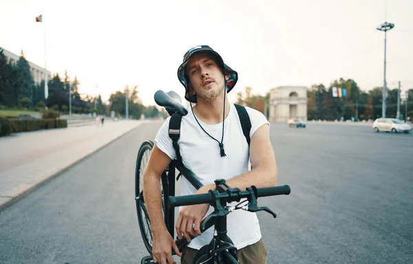 Portrait of a blonde white man in the city with a classic bike on shoulder, looking to camera while standing on a road in the city