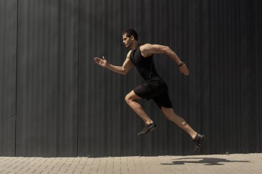 Bir tarafı uygun genç, atletik bir adam atlama ve koşu kardiyo aralığı eğitim gri bir arka plan yaparken görüntüleyin. Açık havada sabah egzersiz fitness erkek.