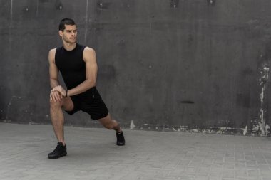 Yakışıklı, atletik bir adam önce arka planda gri duvarlar ile eğitim germe ısınma. Sağlıklı yaşam ve spor giyim reklam.