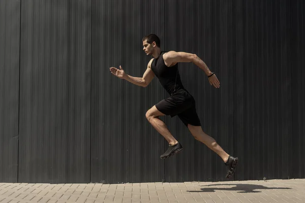 A side view shot of a fit young, athletic man jumping and running doing cardio interval training against a grey background. Fitness male exercising, outdoors in the morning.