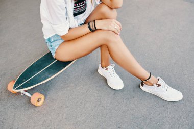 Kadın bacak longboard üzerinde beyaz spor ayakkabı içinde yakın çekim 