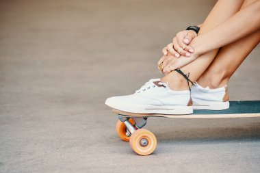 Kadın bacak longboard üzerinde beyaz spor ayakkabı içinde yakın çekim 