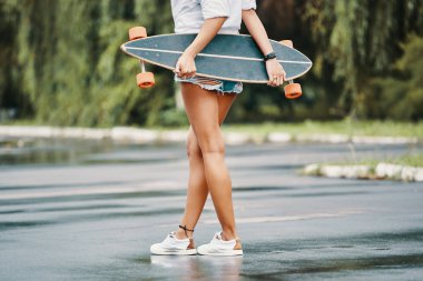 Patenci kız ayakta arkadan görünüş onun longboard onun arkasından tutarak bacak bacak