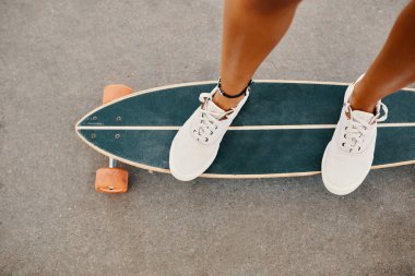 Kadın bacak longboard üzerinde beyaz spor ayakkabı içinde kapatın. Asfalt üzerinde boşaltmak.