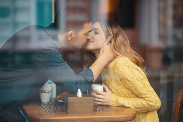 キスをし お互いに過ごした時間を楽しんでいるコーヒー ショップで日付の若い魅力的なカップル 都市の建物を反映して窓から撮影します — ストック写真