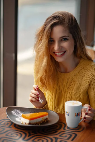 漂亮的年轻女子享受一杯咖啡和一片美味的蛋糕 而休息 阳光透过窗户在咖啡馆里闪耀 — 图库照片