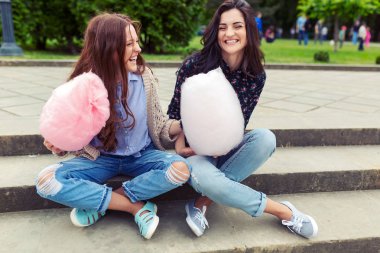 Genç, neşeli kızlar eğleniyor pamuk şeker ile açık havada kentsel arka plan üzerinde. İki kız kardeş komik suratlar ve bıyıklı oynama ve pamuk şeker yemek yapma