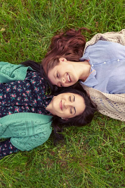 微笑的朋友躺在草地上玩得开心 用手闭上眼睛的最高视野 姐妹们花时间在一起 — 图库照片