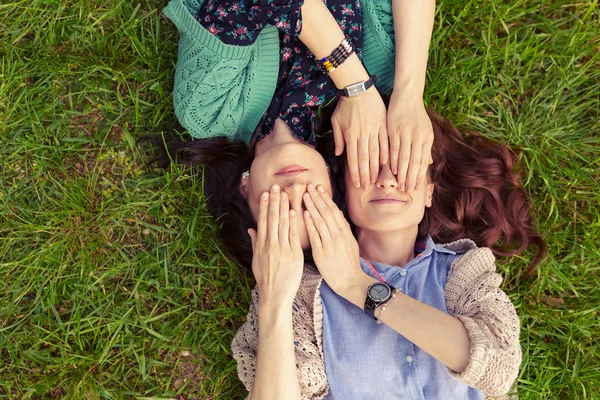 Üstten görünüm gülümseyen arkadaş eğleniyor, elleriyle gözlerini kapatma çim üzerinde yalan. Birlikte vakit kardeş.