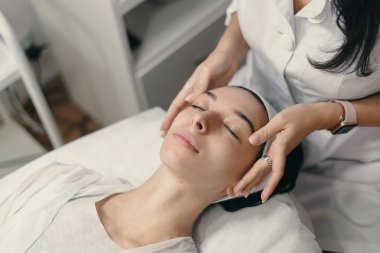 Güzellik, spa ve kozmetik kavramı. Genç kadın kapalı gözler ile yüz cilt gençleştirme, yüz için prosedür Masaj yapma güzellik uzmanı yatıyor..