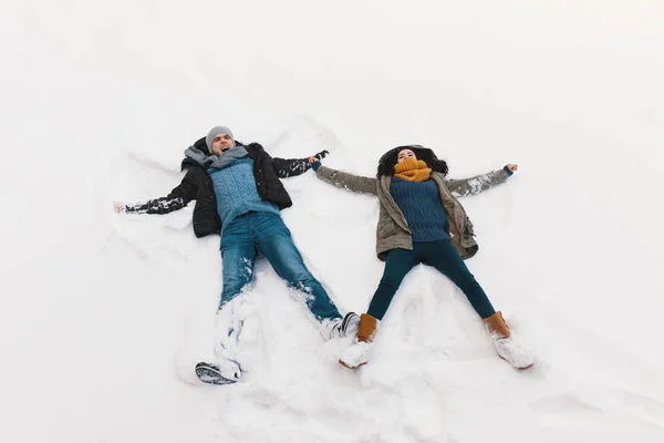 无忧无虑的女人和男人在白色的雪中玩耍 而在冬天的时候 她躺在户外飞翔的天使的位置上 — 图库照片