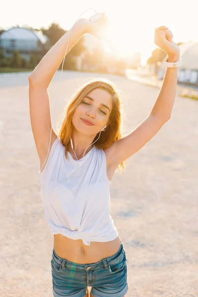 Радісна Дівчина Танцює Вулиці Сонячний День Тримаючи Руки Смартфонами Навушниками — стокове фото