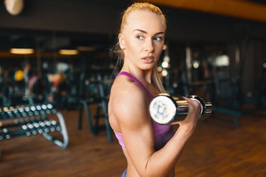Eğitim silah spor yaparken dumbbells ile egzersiz yaparak beyaz bir genç kadın. Güç ve motivasyon kavramı. Yan görünüm 