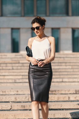 Bir kahverengi deri kalem etek ve krem ipek bluz, merdivenlerde sokakta yürürken güneş gözlüğü moda esmer işkadını. Moda bahar, yaz fotoğraf. Uzun bacakları