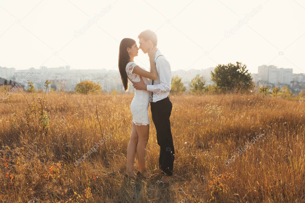 Loving couple dressed in white kissing outdoors, touching, gentle each other with a beautiful landscape in background, golden grass - Concept about people, love and lifestyle