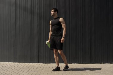 Elinde bir su şişesi ile gri metalik duvara poz atletik modern genç adam. Hidrasyon ve beslenme 's kavramı. Fitness kaslı erkek. İnsan dağ güç pozlar.