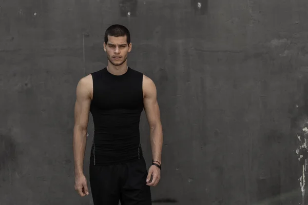 Portrait of athletic muscular young man, in sports clothing, posing on gray industrial background. Fashionable tall male, sport model, muscular body shape, healthy lifestyle advertisment.