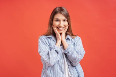 Şık olumlu güzel şirin, Sevimli güzel çekici kız rahat gömlekli, açılan ağız, uzun saçlı portresi holding yanakları kırmızı üzerinde izole, palms