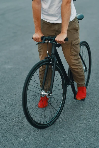 特写的休闲男子腿骑经典自行车在城市灰色的道路上穿着红色运动鞋和舒适的裤子 复制空间 — 图库照片