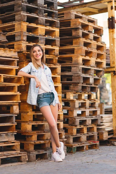 Chica bastante sonriente, con pantalones vaqueros, pantalones cortos y camisa posando sobre fondo de madera —  Fotos de Stock