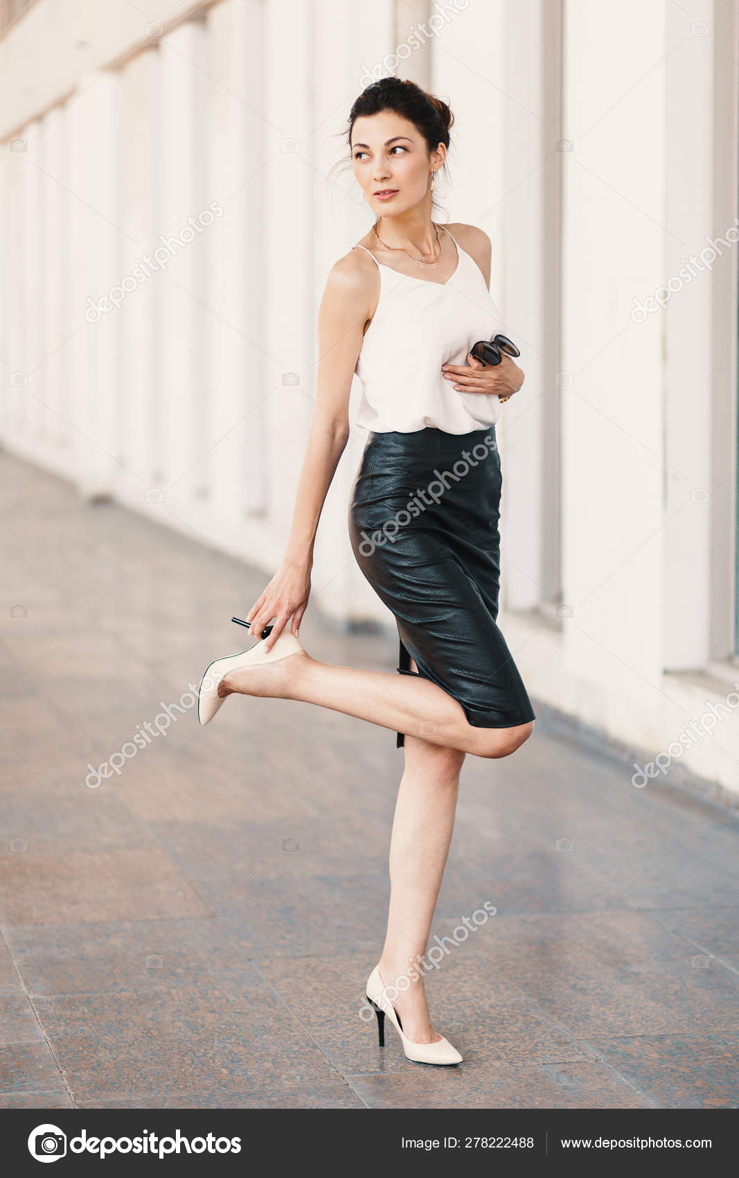 Tall woman touching the black heel on her nude shoe while ...