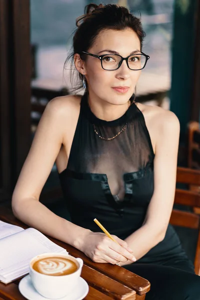 Jovem mulher elegante com óculos elegantes sentados à mesa no café com uma grande xícara de café ou latte — Fotografia de Stock