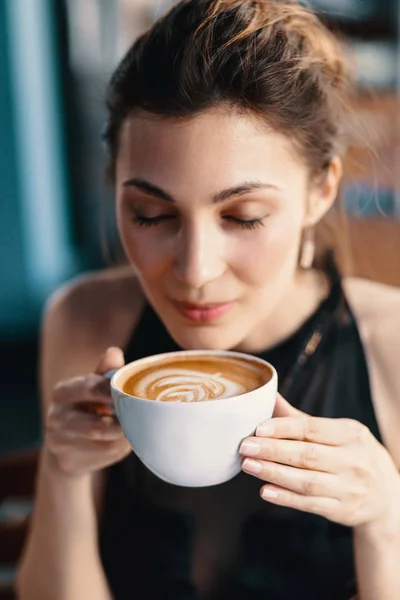 Kifinomult nő élvező cappuccino vagy latte egy élénk, színes háttér beltéri. — Stock Fotó