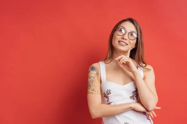 Mulher caucasiana com óculos de pensamento e imaginação isolada no fundo vermelho — Fotografia de Stock