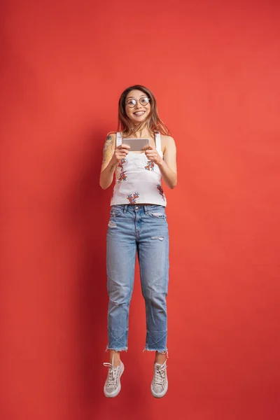 Überraschte junge Frau immer auf Handy auf rotem Hintergrund — Stockfoto