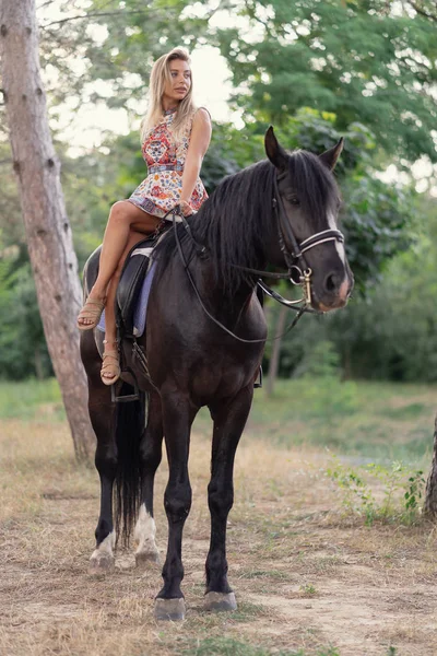 Mujer joven en un vestido colorido brillante montando un caballo negro —  Fotos de Stock
