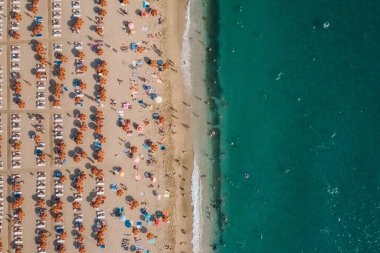 Deniz kenarındaki kumsalda dinlenen insanların hava görüntüsü.