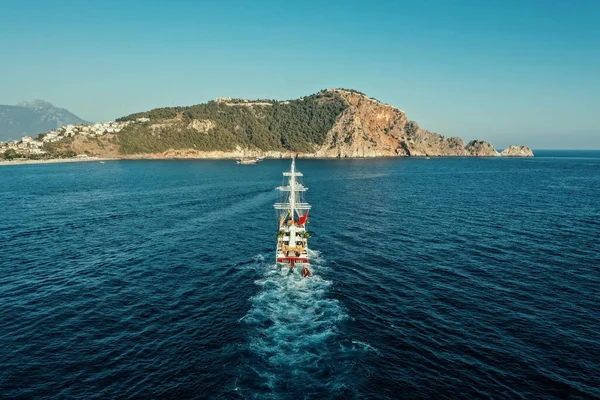 Aerial view of yacht on the sea in motion to rocky mountain with vegetation