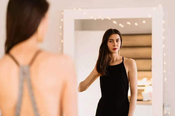 Señora lleva hermoso vestido negro mirando en el espejo — Foto de Stock