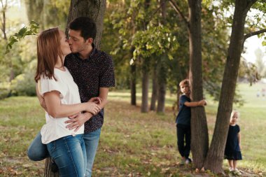 Çocukları dışarıdayken öpüşen çiftler.