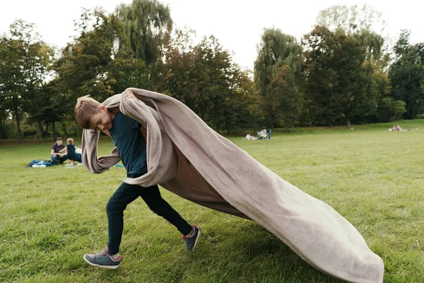 快乐的男孩拿着毛毯在公园里跑来跑去 — 图库照片