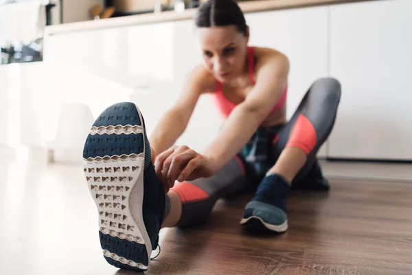 Mulher amarrando seus sapatos esportivos enquanto sentada no chão — Fotografia de Stock