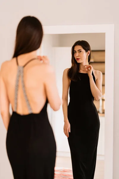 Señora lleva hermoso vestido negro mirando en el espejo — Foto de Stock