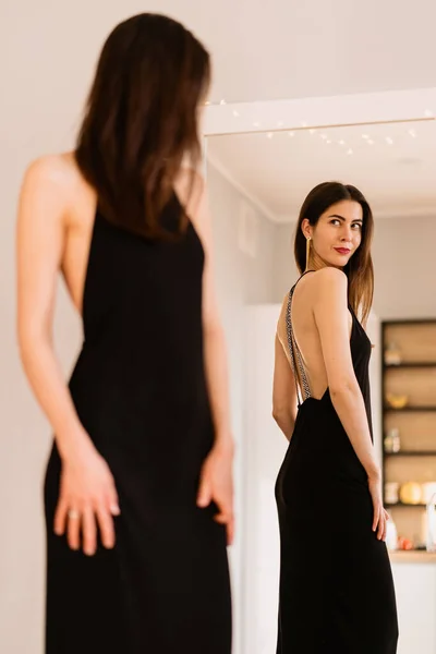 Lady trägt schönes schwarzes Kleid und schaut in den Spiegel — Stockfoto